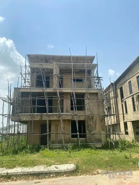 The front of a three-storey 5-bedroom detached duplex carcass in Idu, Abuja, plastered, with bamboo scaffolding and grass in front