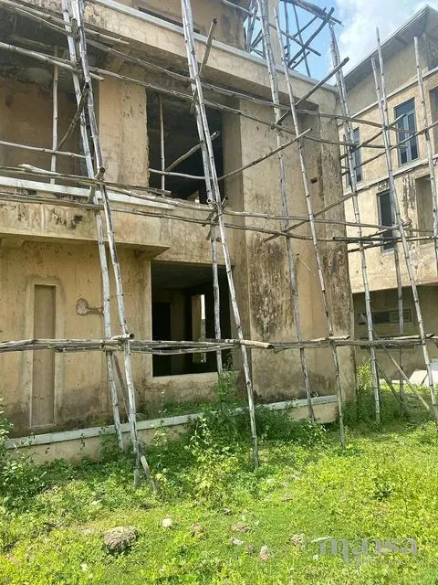 The plastered front of the carcass behind bamboo scaffolding, with grass in front