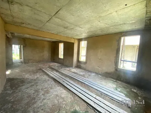 A large unfinished ground-floor space with plastered walls and a concrete ceiling