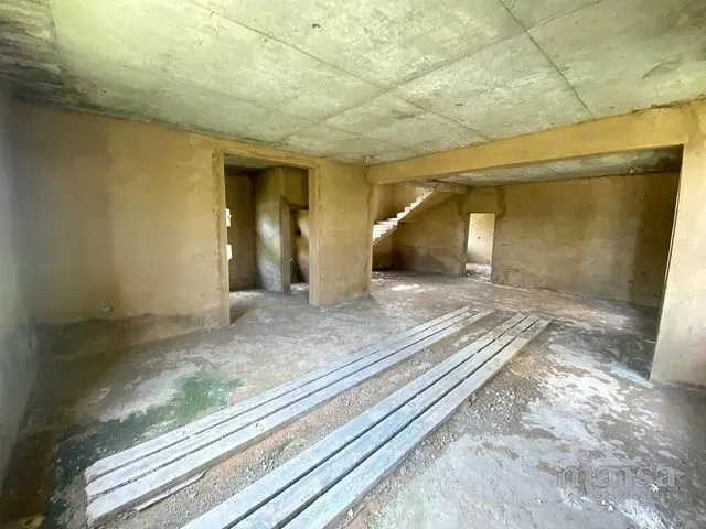 A large unfinished ground-floor space with a concrete staircase visible through an opening
