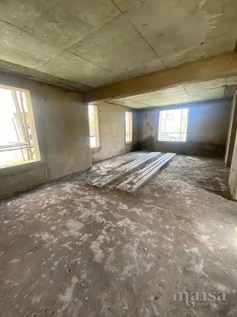 An unfinished room with two window openings looking onto grass