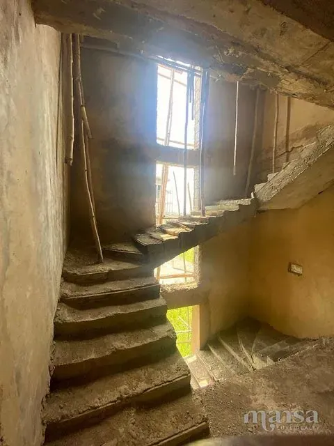 A cast concrete staircase in a plastered stairwell lit by tall windows