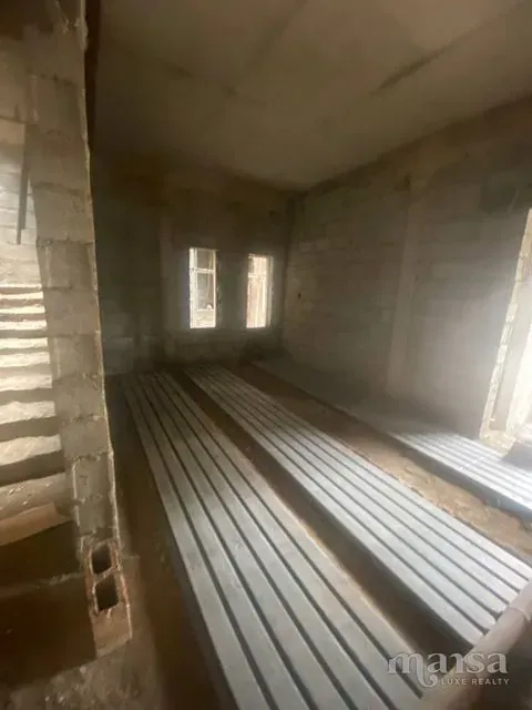 A long unfinished ground-floor room with bare block walls and concrete staircase to one side