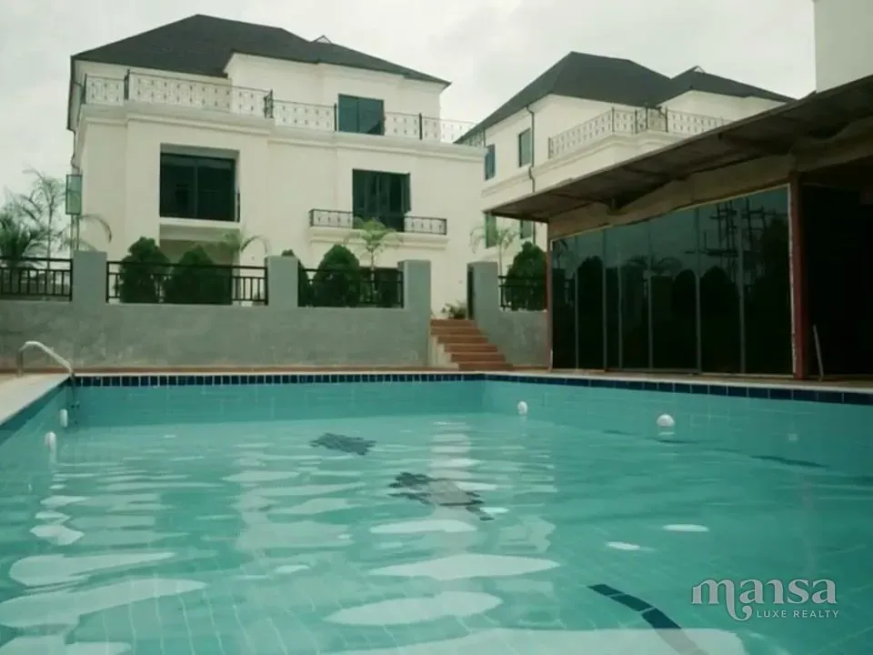 A swimming pool in front of a white detached duplex with dark window frames in a mini estate in Katampe Extension, Abuja