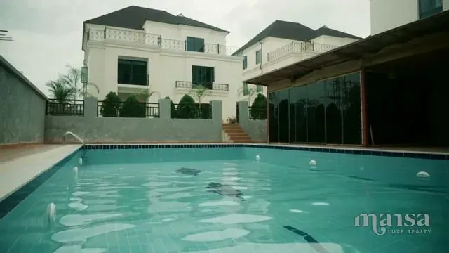 A swimming pool in front of a white detached duplex with dark window frames in a mini estate in Katampe Extension, Abuja