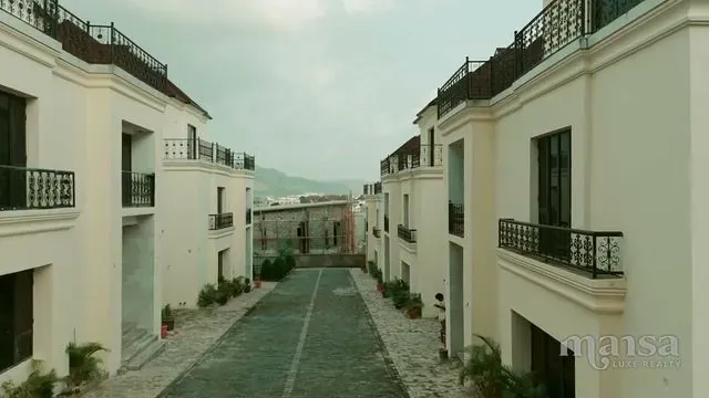 A paved estate road running between white detached duplexes with balconies on each floor