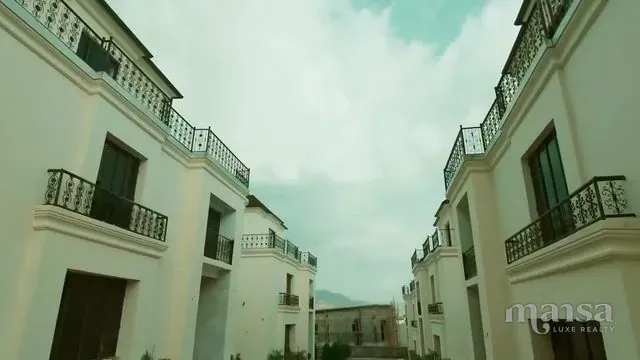White detached duplexes with black balcony railings on both sides of an estate road